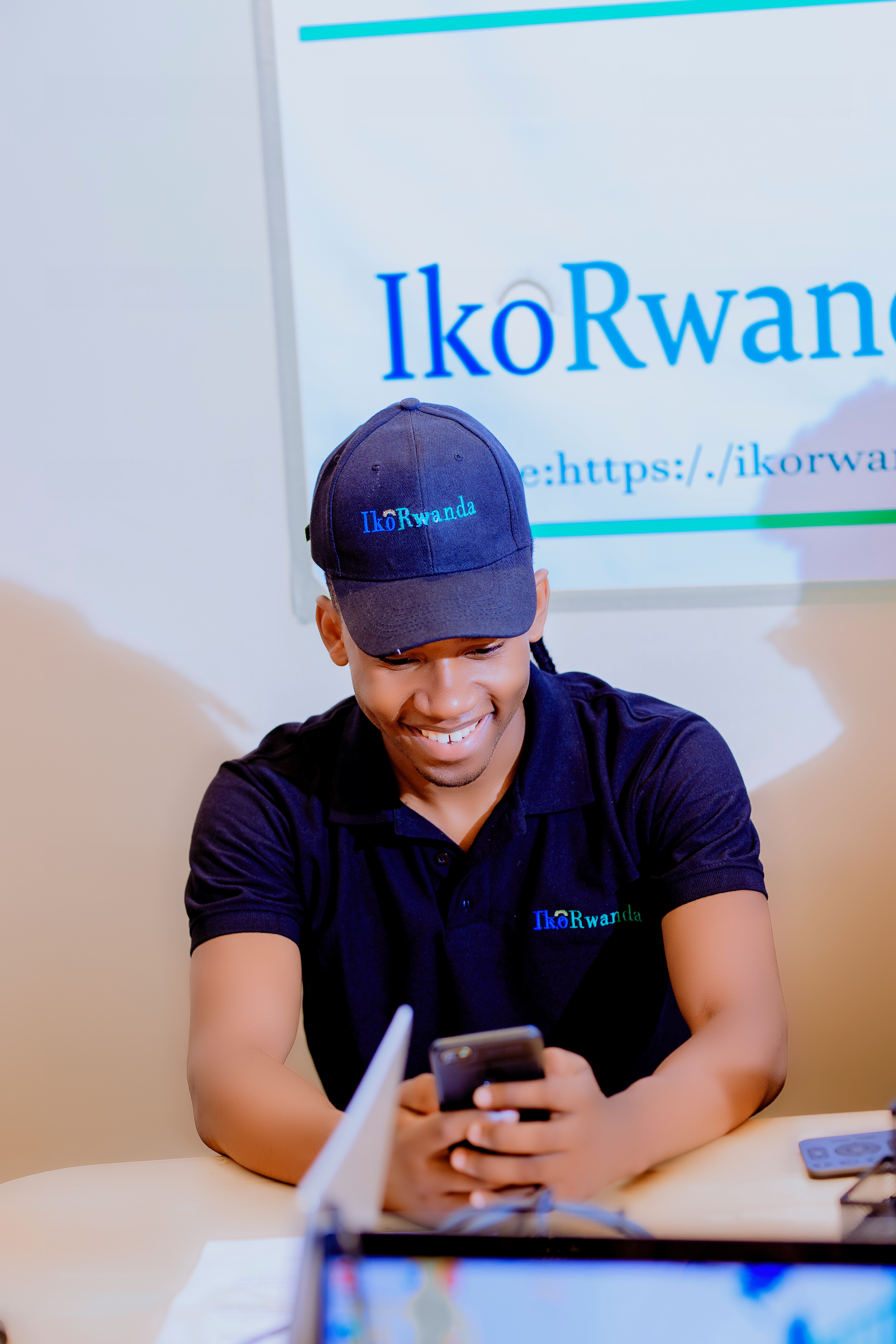 Team member in IkoRwanda branded cap smiling while working at laptop